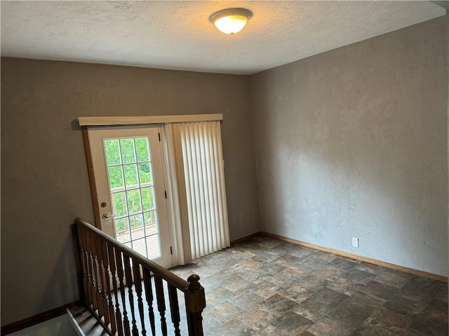 empty room with a textured ceiling, stone finish flooring, a textured wall, and baseboards