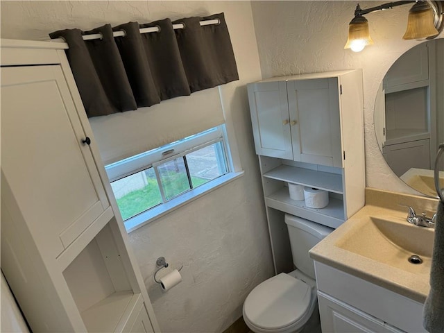 bathroom with toilet, vanity, and a textured wall