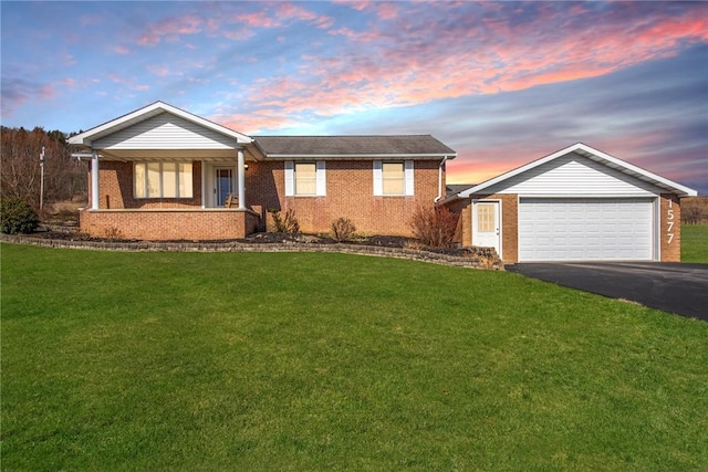 single story home with a garage, aphalt driveway, covered porch, a yard, and brick siding