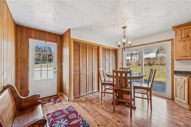 dining room with a chandelier, wood walls, and light wood-style floors