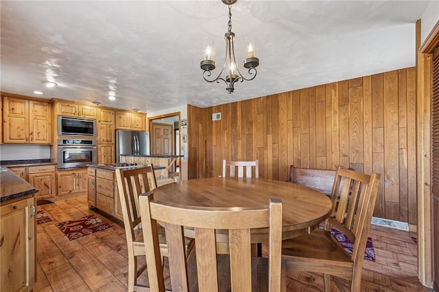 dining room with light wood-type flooring, a notable chandelier, and wooden walls