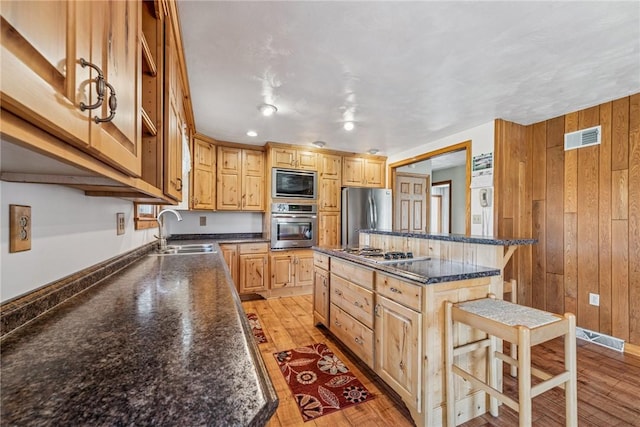 kitchen with stainless steel appliances, visible vents, a sink, wooden walls, and a kitchen breakfast bar