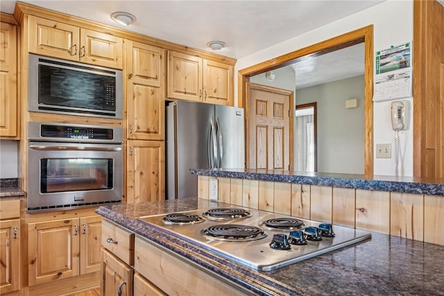 kitchen featuring dark stone counters, stainless steel appliances, and light brown cabinetry