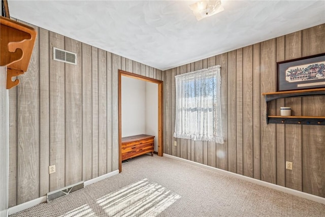 unfurnished room featuring wood walls, carpet, and visible vents