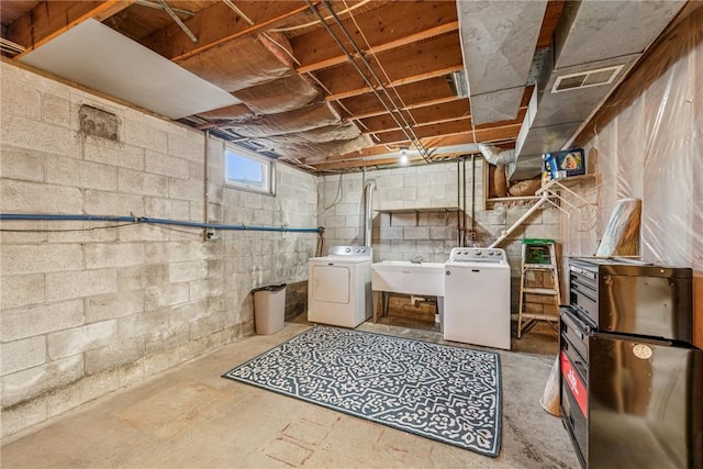 basement with a sink, washing machine and clothes dryer, and visible vents