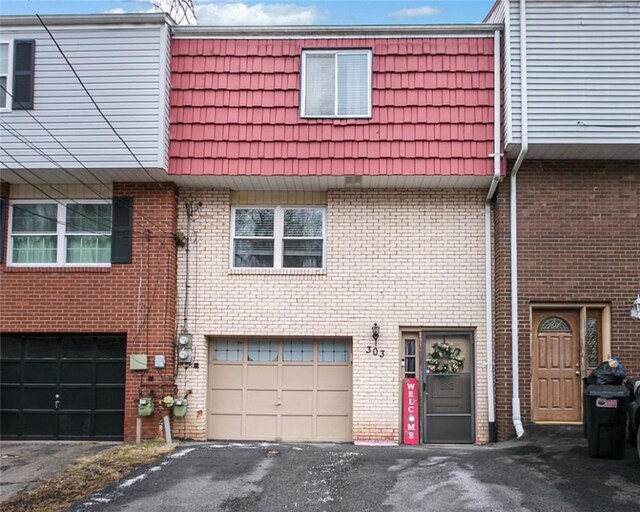 multi unit property featuring a garage, driveway, mansard roof, and brick siding