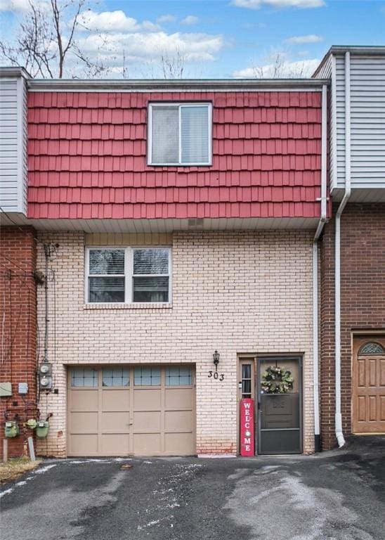 view of front of property featuring an attached garage, driveway, mansard roof, and brick siding
