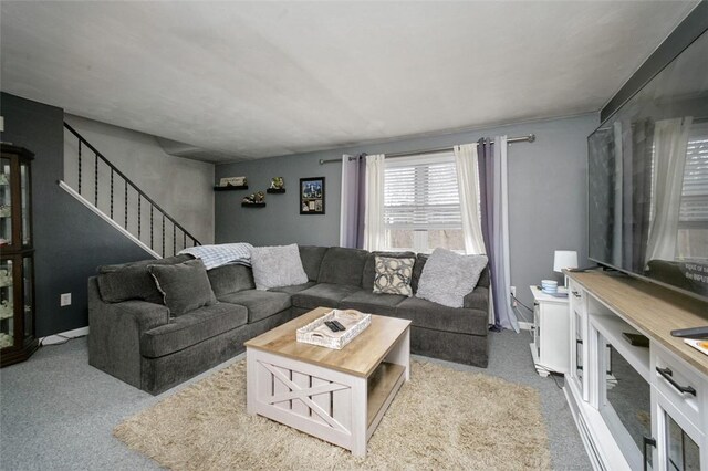 carpeted living area with baseboards and stairs