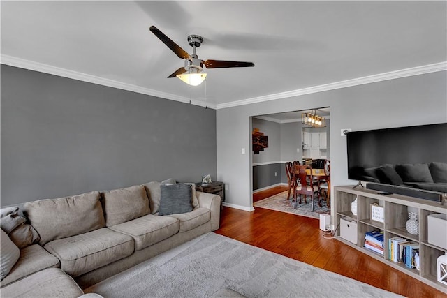 living area with crown molding, baseboards, wood finished floors, and ceiling fan with notable chandelier