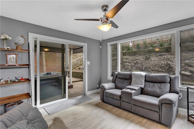 living area with a ceiling fan, plenty of natural light, baseboards, and wood finished floors