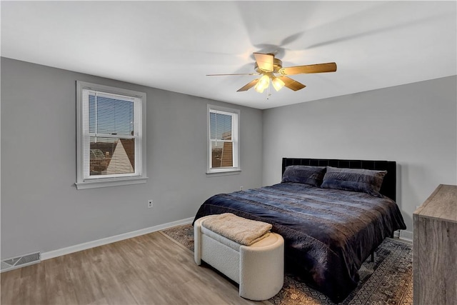 bedroom with baseboards, multiple windows, visible vents, and wood finished floors