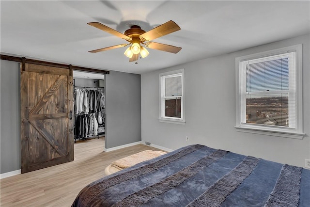 unfurnished bedroom featuring ceiling fan, a spacious closet, baseboards, and wood finished floors