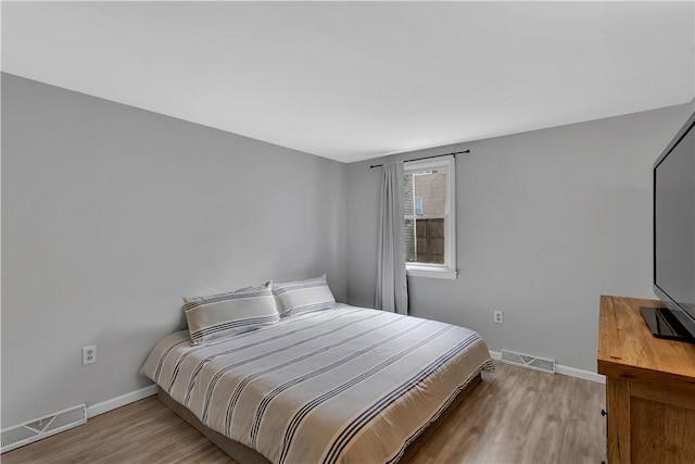 bedroom with baseboards, visible vents, and wood finished floors