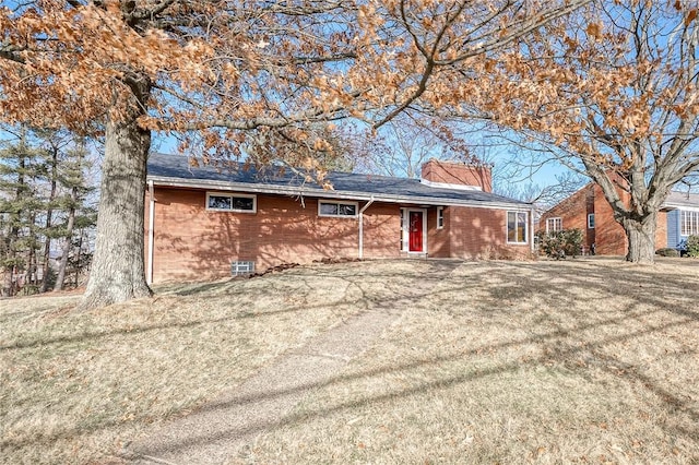 single story home featuring brick siding, a chimney, and a front yard