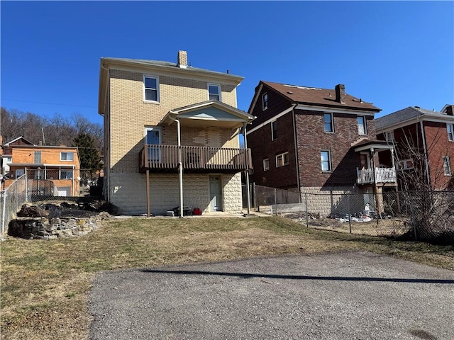 rear view of house with brick siding, a chimney, and fence