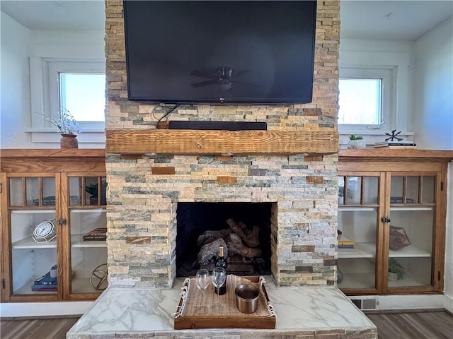 room details with ceiling fan, a stone fireplace, wood finished floors, and visible vents