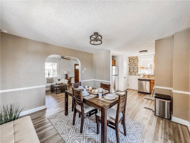 dining room featuring arched walkways, a textured ceiling, and light wood finished floors