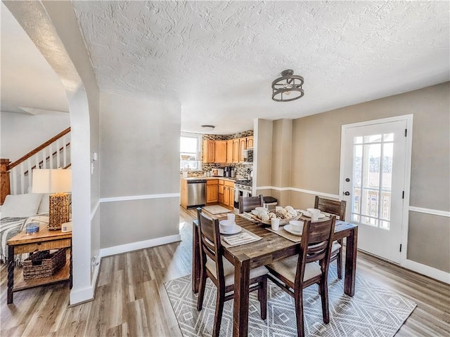 dining space featuring plenty of natural light, light wood-style flooring, baseboards, and a textured ceiling