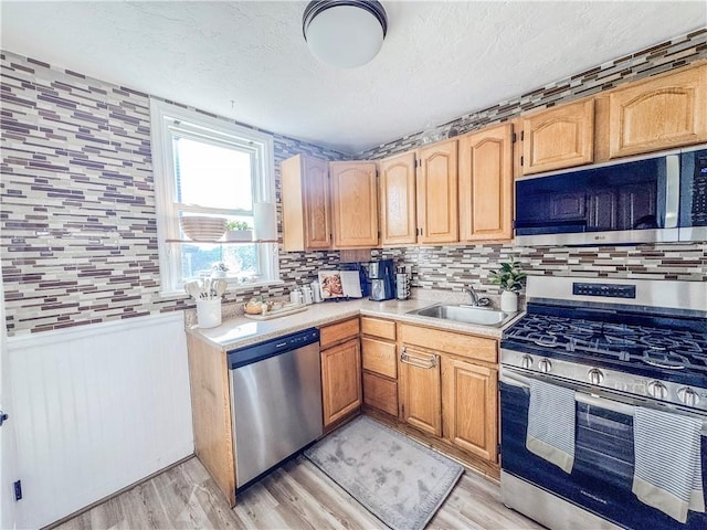 kitchen with stainless steel appliances, wainscoting, a sink, and light countertops