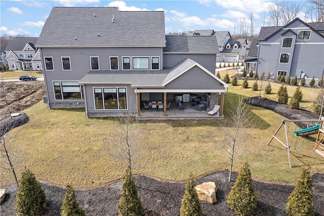 back of property featuring a yard, a residential view, a playground, and a patio