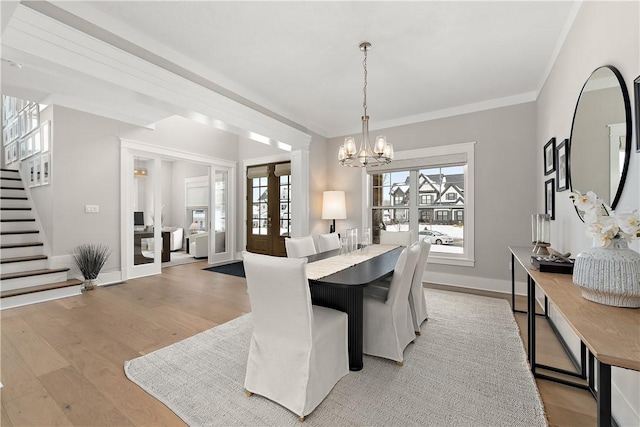 dining area featuring stairway, crown molding, french doors, light wood-style floors, and a chandelier