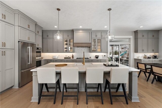 kitchen featuring stainless steel appliances, premium range hood, a kitchen bar, and gray cabinets