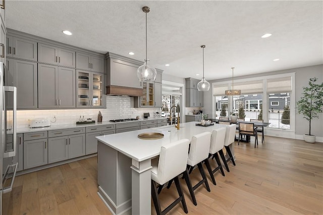 kitchen with light wood-type flooring, gray cabinets, and custom range hood