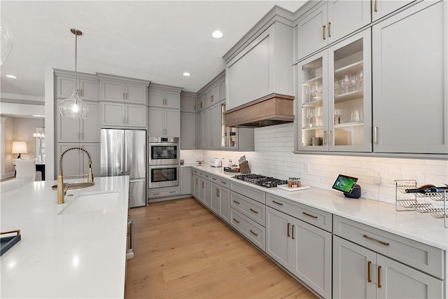 kitchen featuring gray cabinetry, stainless steel appliances, light wood-style floors, decorative backsplash, and glass insert cabinets