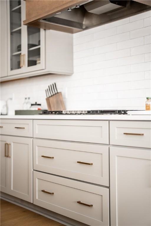 kitchen featuring light countertops, wall chimney range hood, dark wood-type flooring, and glass insert cabinets