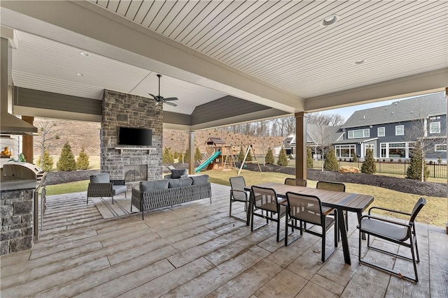 view of patio / terrace featuring area for grilling, fence, an outdoor stone fireplace, a playground, and outdoor dining space