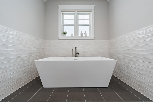 bathroom with tile patterned flooring, wainscoting, a freestanding bath, and tile walls