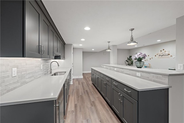 kitchen with tasteful backsplash, recessed lighting, light countertops, light wood-style floors, and a sink