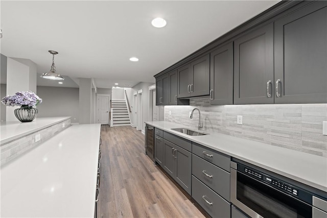 kitchen with dishwashing machine, a sink, light countertops, decorative backsplash, and light wood finished floors