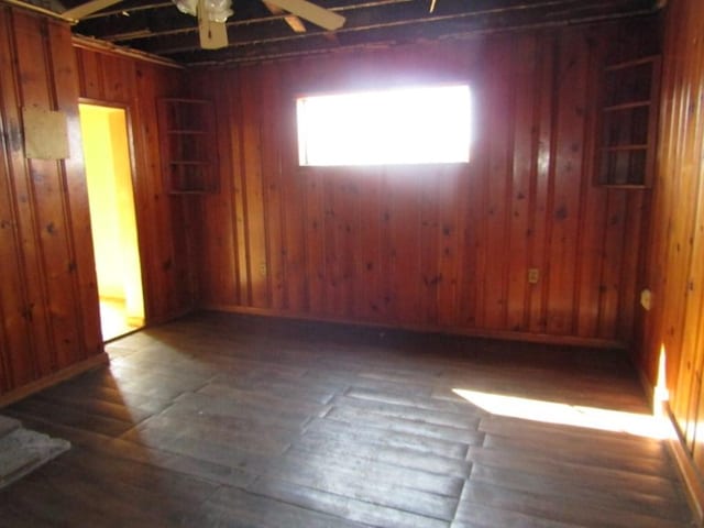 spare room with wood walls, a ceiling fan, and wood finished floors