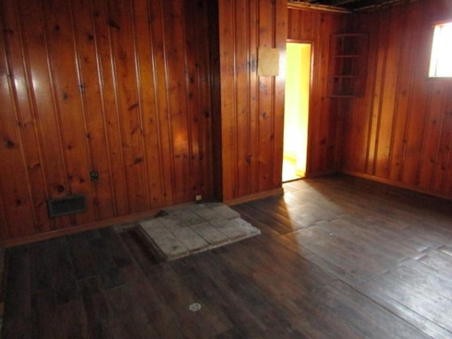 spare room featuring visible vents, wooden walls, baseboards, and hardwood / wood-style flooring