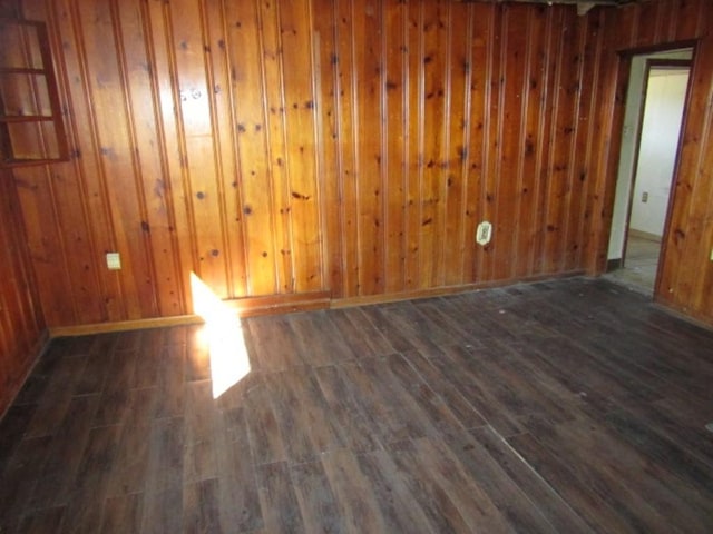 empty room featuring dark wood-style floors, wood walls, and baseboards