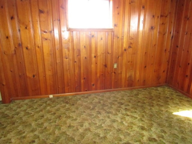 carpeted spare room featuring wood walls and baseboards