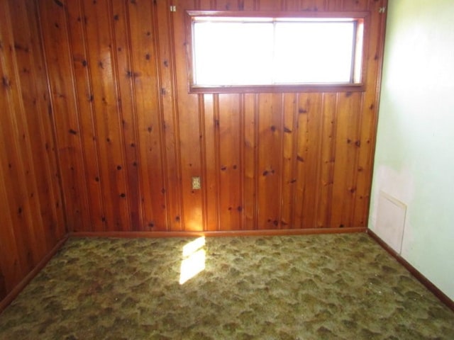 carpeted spare room with visible vents and wooden walls