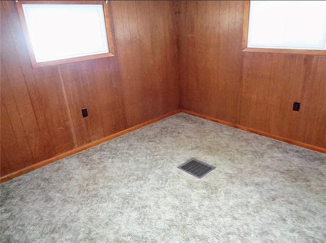 carpeted empty room with visible vents and wooden walls