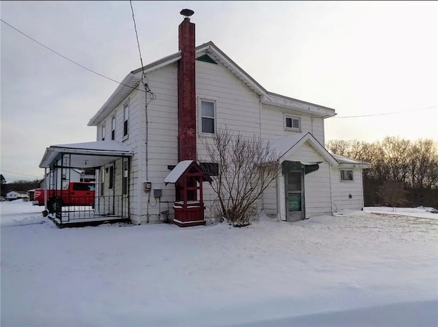 snow covered rear of property with a chimney