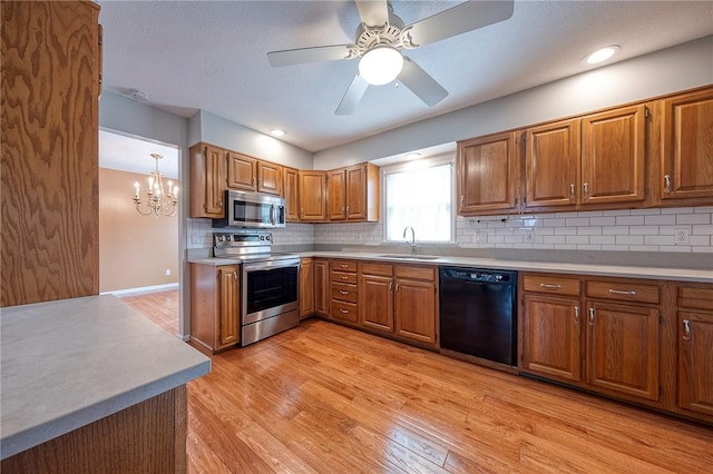 kitchen with appliances with stainless steel finishes, a sink, light wood-style floors, and brown cabinets