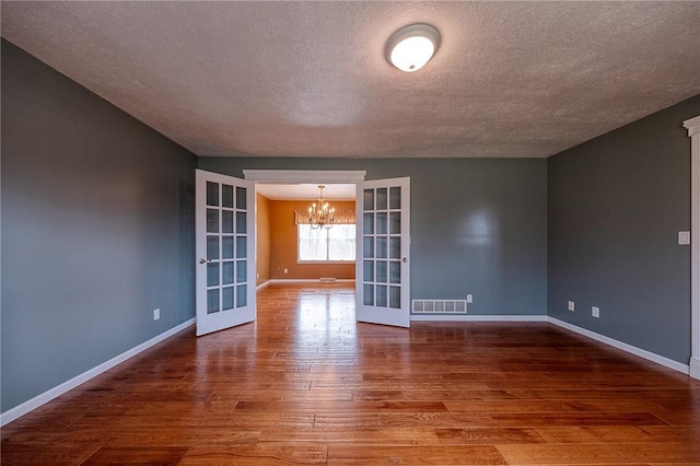 empty room with a notable chandelier, wood finished floors, visible vents, baseboards, and french doors