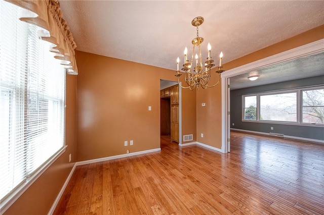 empty room featuring light wood-style floors, visible vents, a notable chandelier, and baseboards