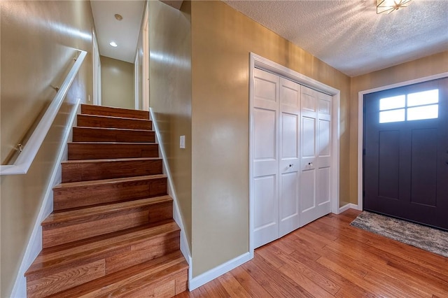 entryway with stairs, a textured ceiling, baseboards, and wood finished floors