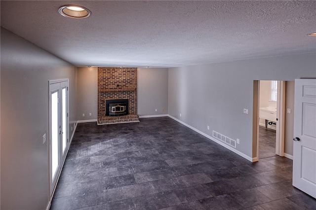 unfurnished living room with baseboards, a fireplace, visible vents, and a textured ceiling