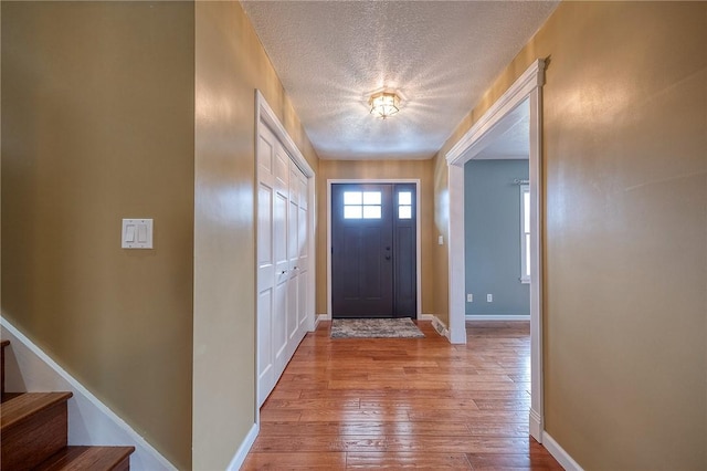 foyer with stairs, a textured ceiling, baseboards, and light wood-style floors