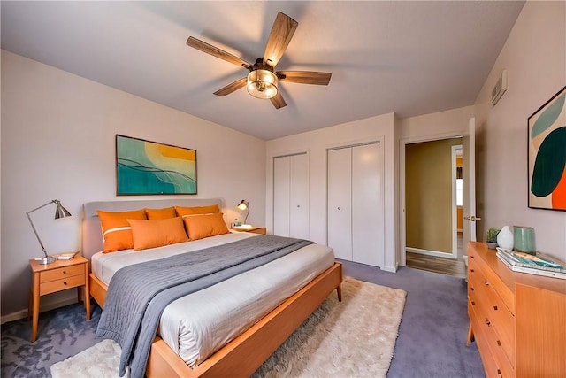 carpeted bedroom featuring multiple closets, visible vents, baseboards, and a ceiling fan