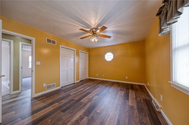 unfurnished bedroom with multiple closets, visible vents, and dark wood finished floors