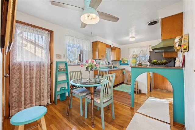 kitchen featuring brown cabinets, light countertops, light wood-style floors, a ceiling fan, and under cabinet range hood