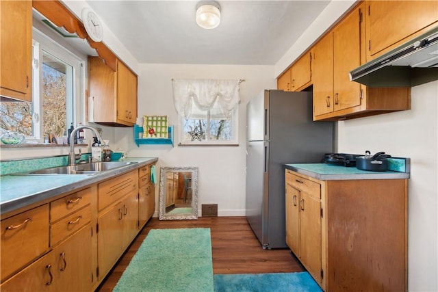 kitchen with dark wood-style flooring, visible vents, freestanding refrigerator, a sink, and under cabinet range hood